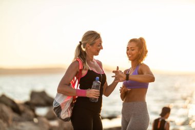 Mother and her adult daughter talking and support each other before training near the sea beach.