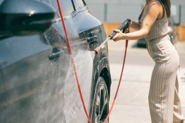 Güneşli bir günde araba yıkayan mutlu kadın..