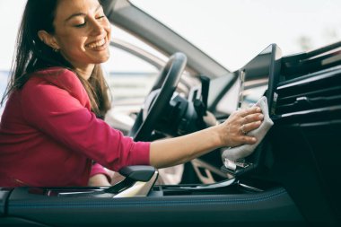 Arabanın içindeki tozları bezle temizleyen genç bir kadın..