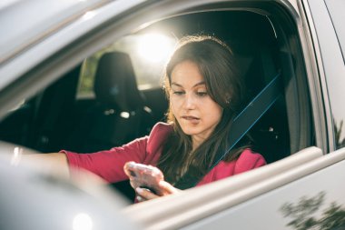 Arabasını sürerken cep telefonuna bakan genç bir kadın..