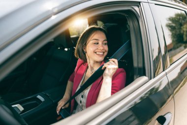 Neşeli genç kadın yeni arabasının emniyet kemerini ayarlıyor..