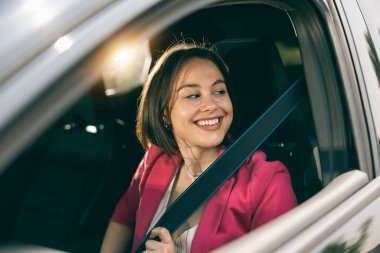 Neşeli genç kadın yeni arabasının emniyet kemerini ayarlıyor..