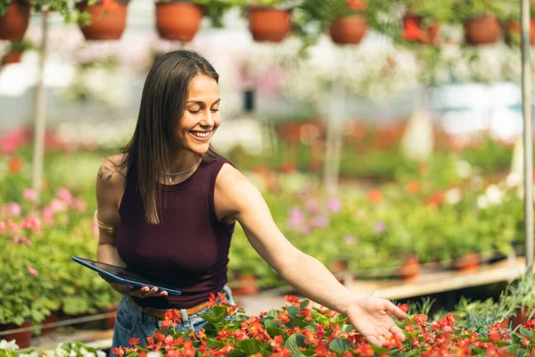 Gülümseyen bir kadın bir tabletle meşgul. Serada canlı çiçeklerle çevrili..