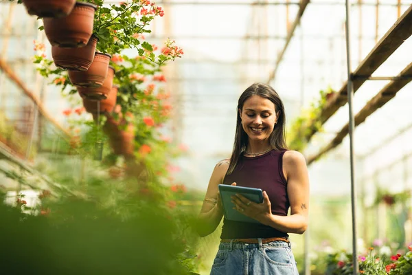 Gülümseyen bir kadın bir tabletle meşgul. Serada canlı çiçeklerle çevrili..