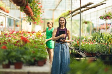 Çiçekçide durup tabletini kullanan neşeli bir genç kadın..
