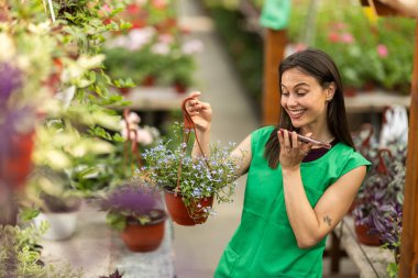 Neşeli, profesyonel bir kadın elinde saksı çiçeği tutarken telefonla iletişim kuruyor..