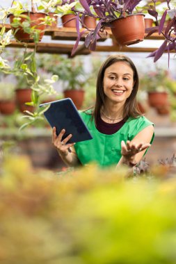 Tabletini kullanırken çiçekçide çalışan neşeli bir kadın..