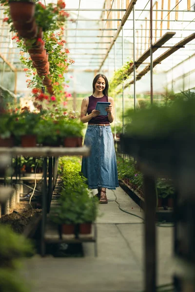 Çiçekçide durup tabletini kullanan neşeli bir genç kadın..