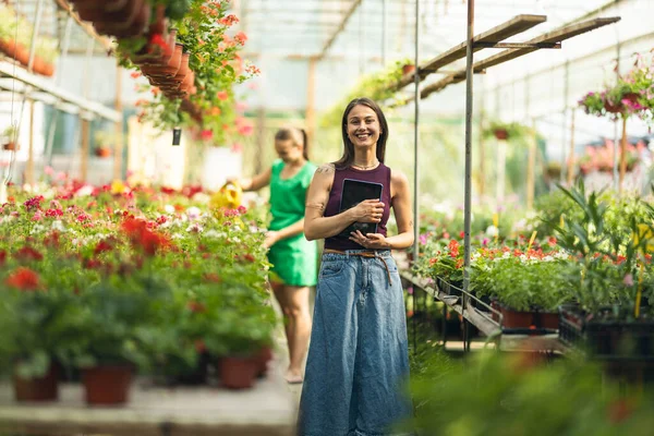 Çiçekçide durup tabletini kullanan neşeli bir genç kadın..