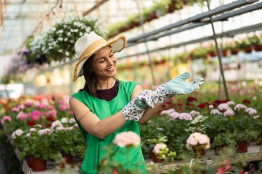Çiçekçide çalışırken eldiven takan neşeli genç bir kadının portresi..