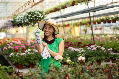 Çiçekçide çalışırken eldiven takan neşeli genç bir kadının portresi..