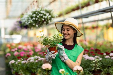 Çiçekçi dükkanında elinde güzel bir çiçek tutan mutlu genç kadın..