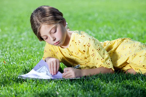 Portrait of little girl studying on the grass in summer environment — Stock Photo, Image