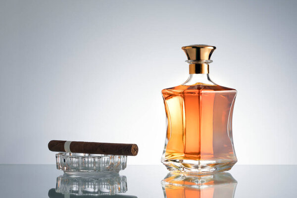close up view of cigar and bottle of congnac aside on grey back. 