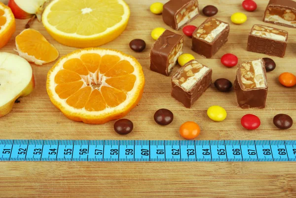 Snoep, vruchten, en een liniaal op een houten bord — Stockfoto