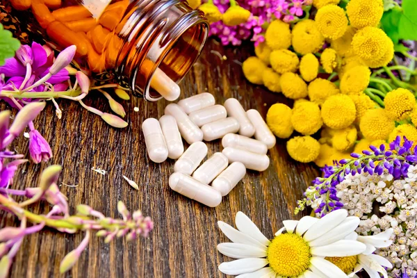 Capsules in brown jar with flowers on dark board — Stock Photo, Image