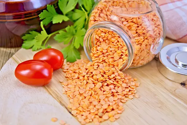 Lentils red in glass jar with tomatoes on board — Stock Photo, Image