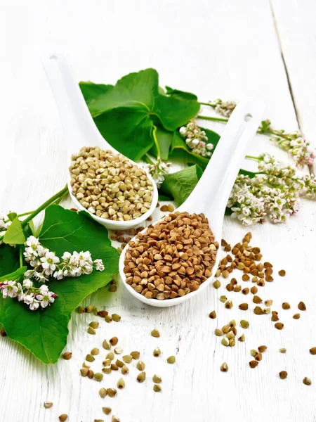 木の板の背景に葉や花を持つ2つのスプーンで茶色と緑のそばの草 — ストック写真