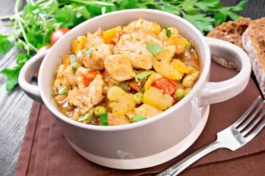 Tavuk göğsü, domates, kereviz, havuç, yeşil bezelye ve soğan güveci kahverengi peçetenin üzerinde koyu ahşap arka planda