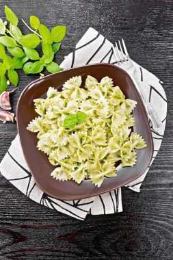 Pesto soslu Farfalle makarna, peçetede fesleğen, tahta tahta arka planda, yukarıdan.