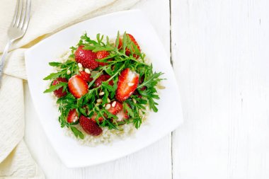 Çilek, kuskus, sedir fıstığı ve balzamik sirke ve tabakta zeytinyağı, peçete ve yukarıdan hafif ahşap arka planda çatal.