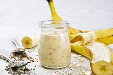 Chia tohumlu milkshake, keten tohumu, yulaf ezmesi, puflanmış pirinç ve muz taştan bir masada cam kavanozda.