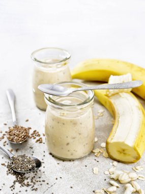Chia tohumlu milkshake, keten tohumu, yulaf ezmesi, puflanmış pirinç ve muz kahverengi granit masa üzerinde iki cam kavanozda.