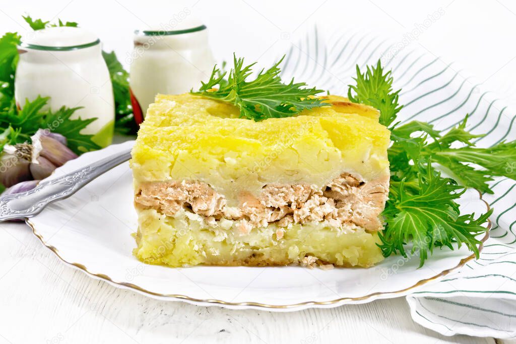 Mashed potato casserole with salmon fillet and lettuce in a plate, towel, garlic on a wooden board background
