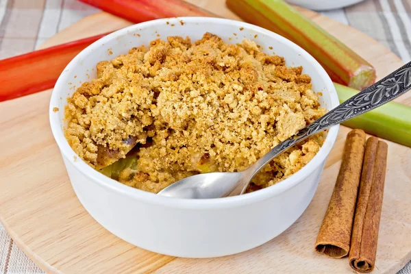 Crumble with rhubarb in bowl on linen tablecloth and board — Stock Photo, Image