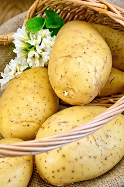 Batatas amarelas em cesta com flor a bordo — Fotografia de Stock