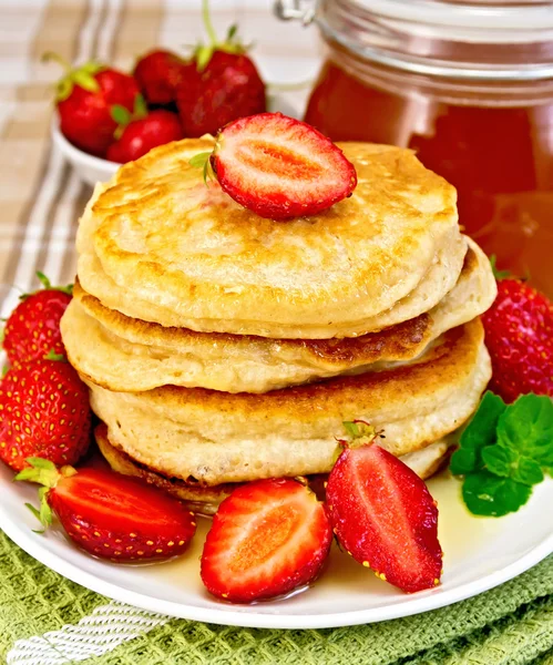 Flapjacks with strawberries and honey on tablecloth — Stock Photo, Image