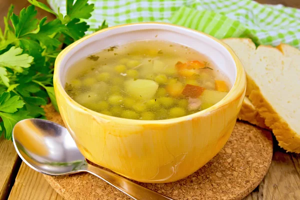 Soup of green peas in yellow bowl with bread on board — Stock Photo, Image