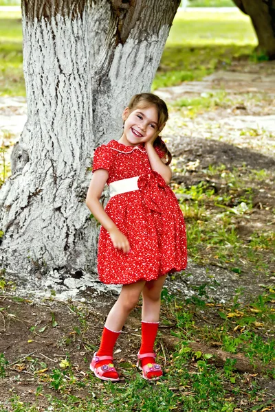 Meisje in een rode jurk onder boom in het park — Stockfoto