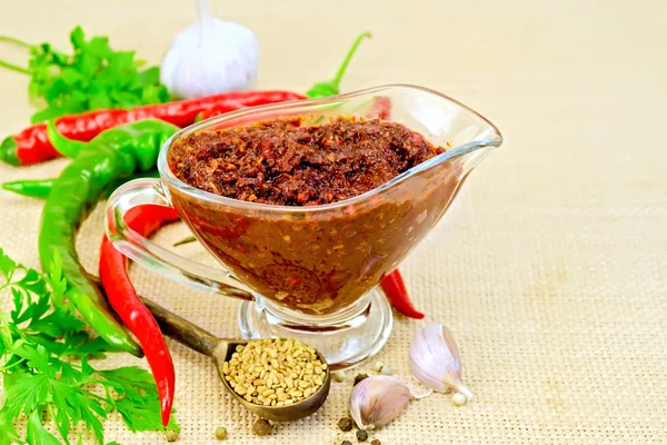 Adjika in glass gravy boat with garlic on sacking — Stock Photo, Image