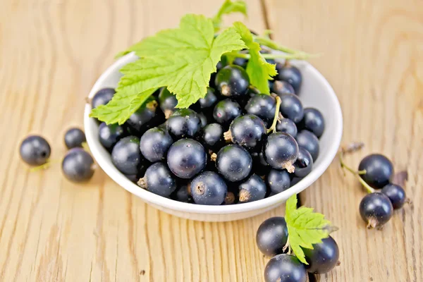 Black currants in bowl with leaf on board — Stock Photo, Image