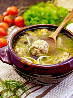 Soup with meatballs and spoon in pottery on napkin