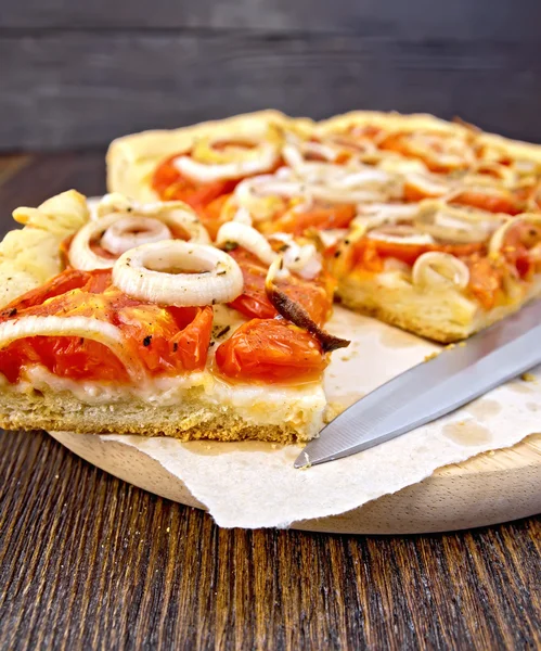 Pie with onions and tomatoes on paper with knife — Stock Photo, Image