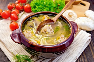 Soup with meatballs and mushrooms in pottery on board
