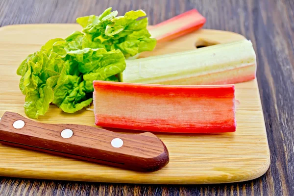 Rhubarb with knife and leaf on board — Stockfoto