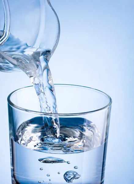 Nahaufnahme, wie man Wasser aus einem Krug auf blauem Grund in ein Glas gießt — Stockfoto