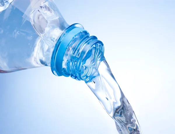 Verser l'eau de la bouteille en plastique sur fond bleu — Photo