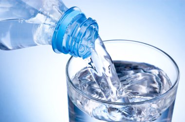 Close-up Pouring glass of water from a plastic bottle on blue ba clipart