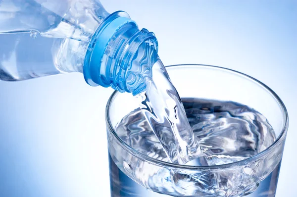 Primer plano Verter un vaso de agua de una botella de plástico sobre una ba azul — Foto de Stock