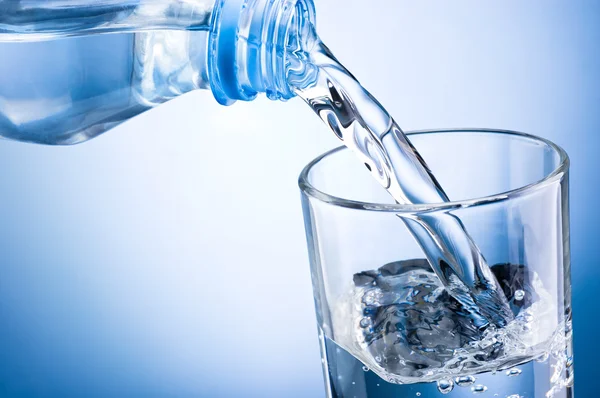 Nahaufnahme, wie man Wasser aus der Flasche in ein Glas auf blauem Grund gießt — Stockfoto