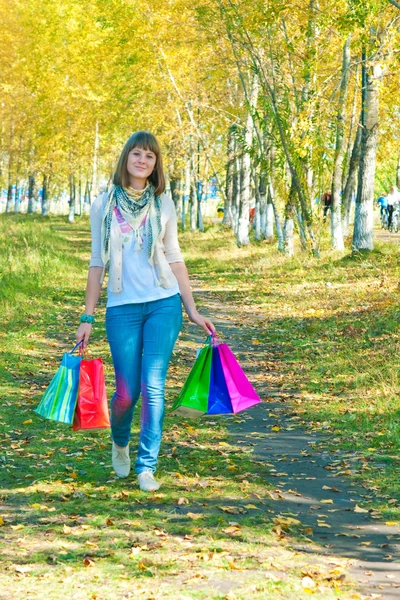 La chica con paquetes multicolores va en el parque — Foto de Stock