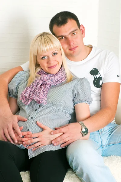 Молодая беременная пара сидит на диване в комнате — стоковое фото