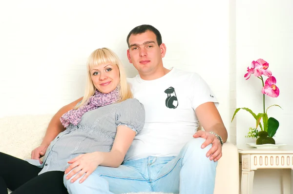 Young pregnant couple sitting on a sofa in a room — Stock Photo, Image