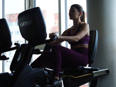 Belarus, Minsk, 2021. Spor salonundaki genç kadın simülatörlerle meşgul.