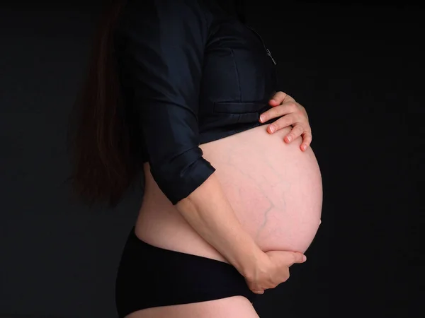 妊娠中の女性は手で腹を暗い背景に置き — ストック写真