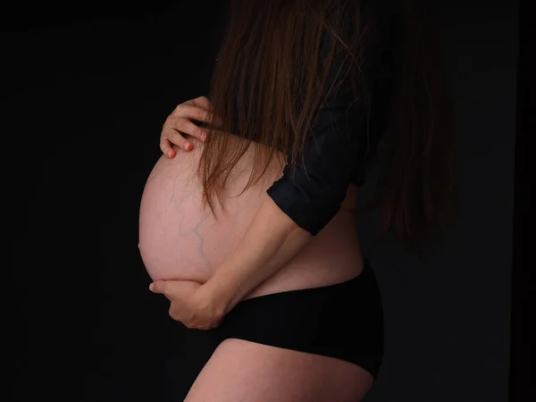 Беременная Женщина Держит Живот Темном Фоне Руками — стоковое фото
